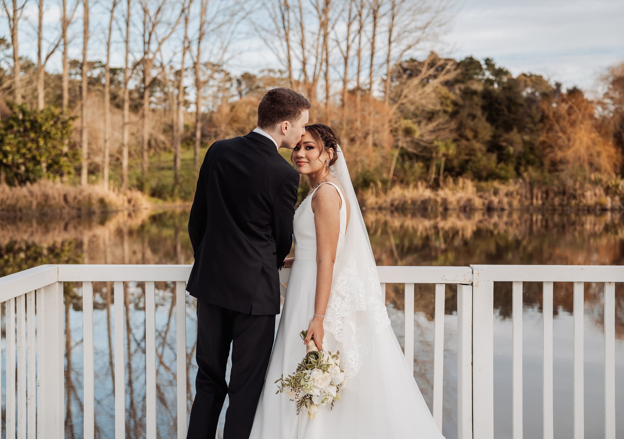 Suzy and James on their wedding day, beside a lake at golden hour